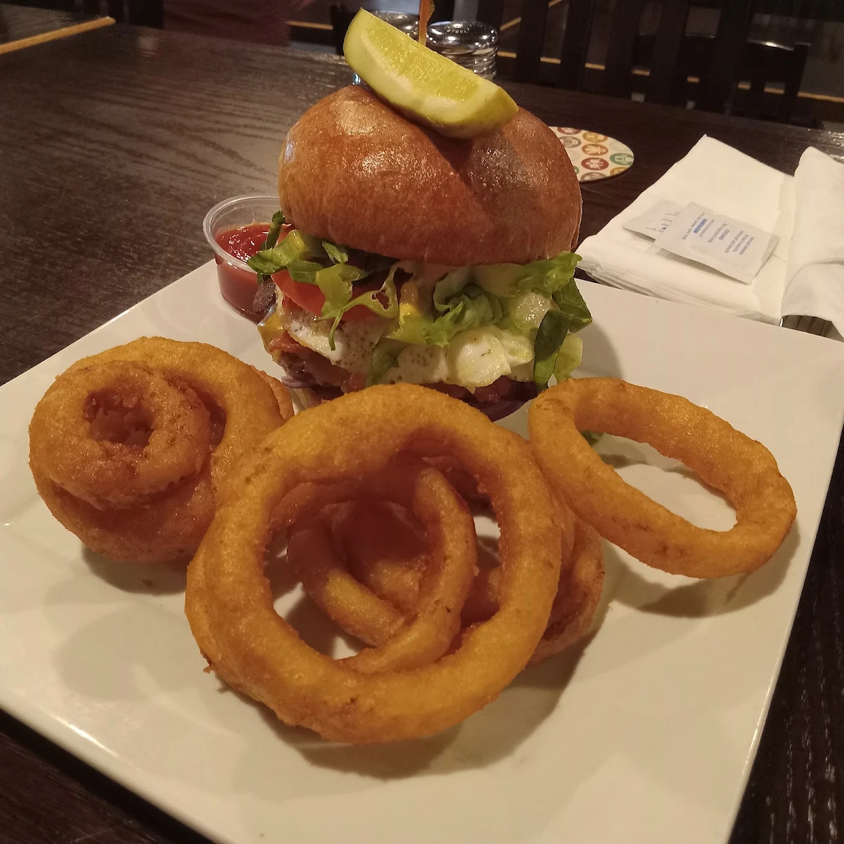 Classic Burger with Cheese Bacon and a Hard Fried Egg on Top with Onion Rings on the Side